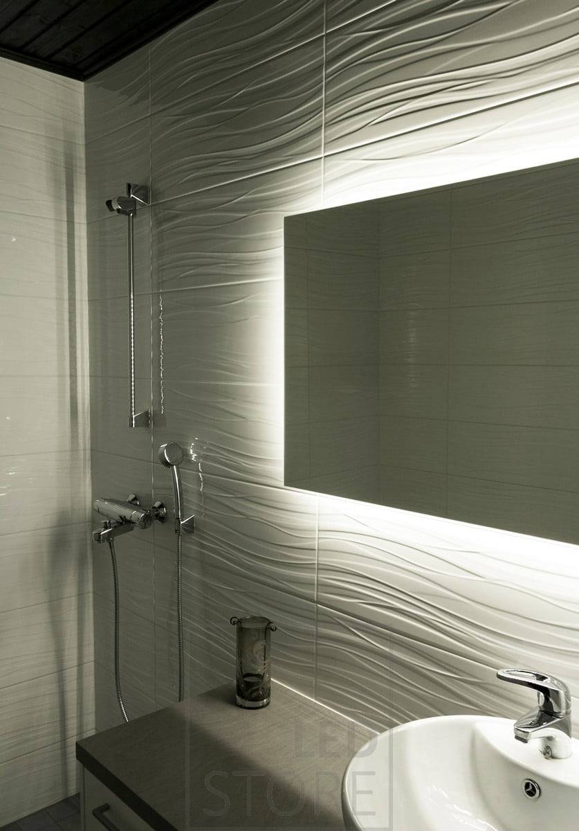 HALO, un gran espejo rectangular luminoso, ilumina a través de la pared, resaltando el azulejo texturizado y añadiendo ambiente al cuarto de baño. Ledstore.fi