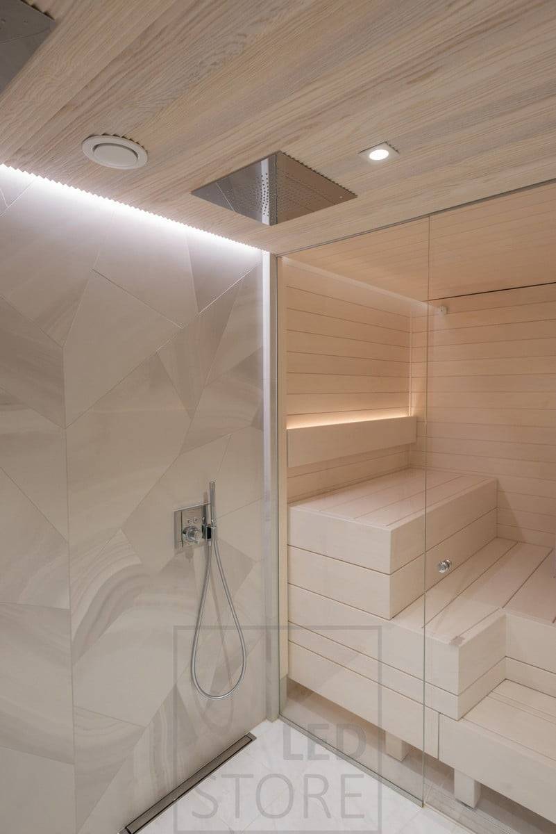 Luz indirecta en el lavabo y la sauna. En el lavabo, en el techo, en una ranura entre el techo y la pared; en la sauna, en el respaldo, orientada hacia arriba. Además, iluminación puntual en el techo delante de las duchas. Ledstore.fi