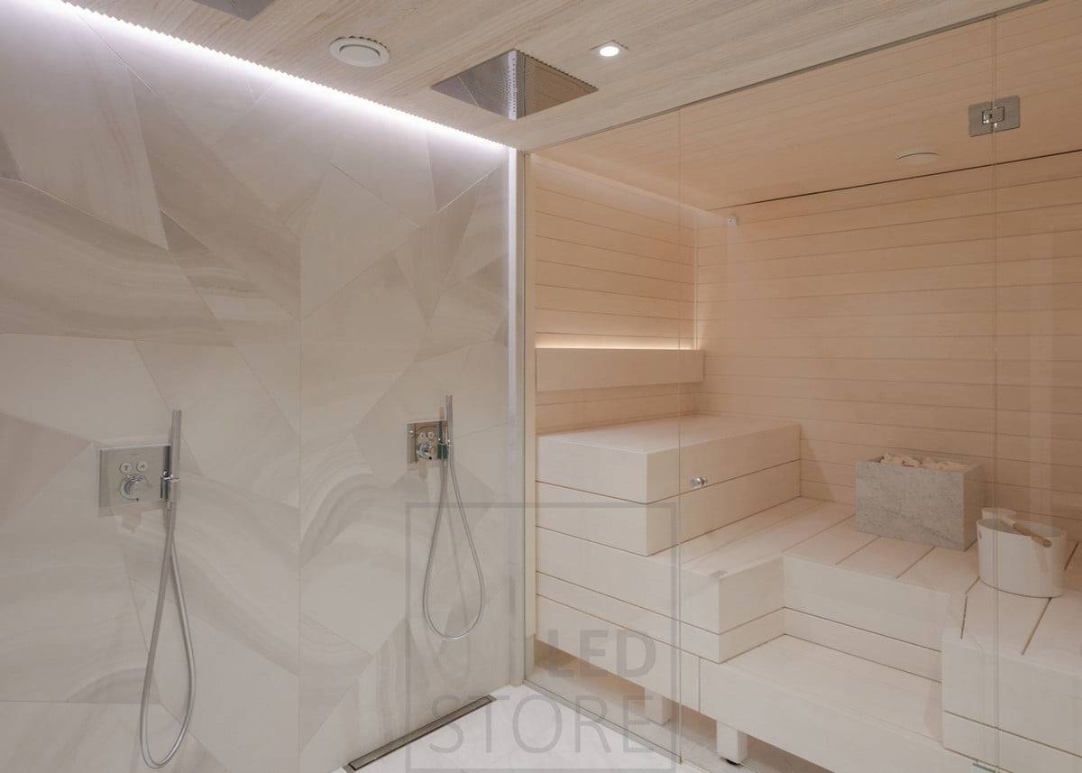 Luz indirecta tanto en el lavabo como en la sauna. En el lavabo, en el techo, en una ranura entre el techo y la pared; en la sauna, en el respaldo, orientada hacia arriba. La luz del lavabo también ilumina la sauna gracias a las paredes de cristal. Ledstore.fi