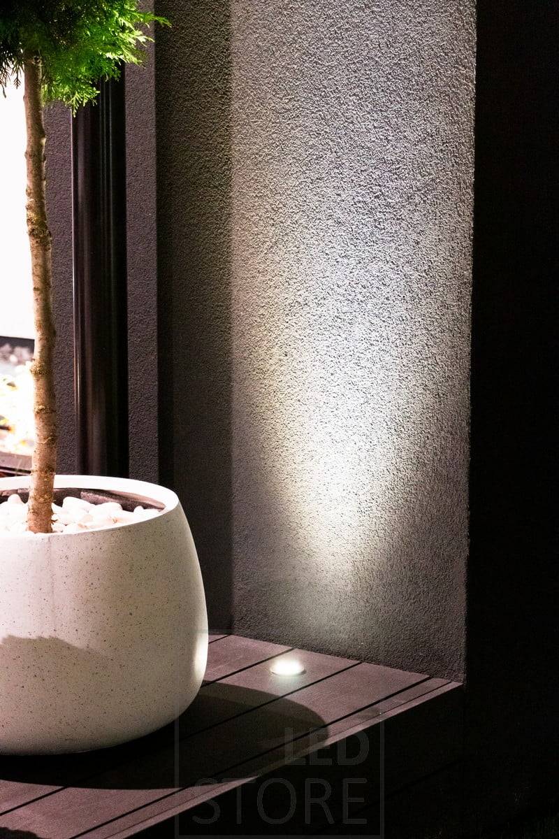 Foco de luz ascendente empotrado en la terraza, que ilumina a través de la pared. La luz también resalta maravillosamente la planta de delante. Ledstore.fi