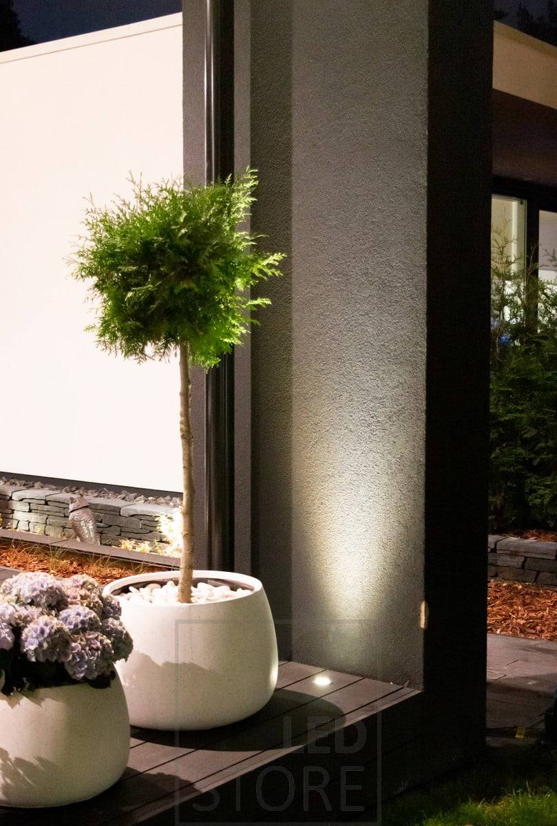 Un foco de luz ascendente empotrado en una terraza utiliza la pared como superficie reflectante. La luz también resalta bellamente la planta de enfrente. Ledstore.fi