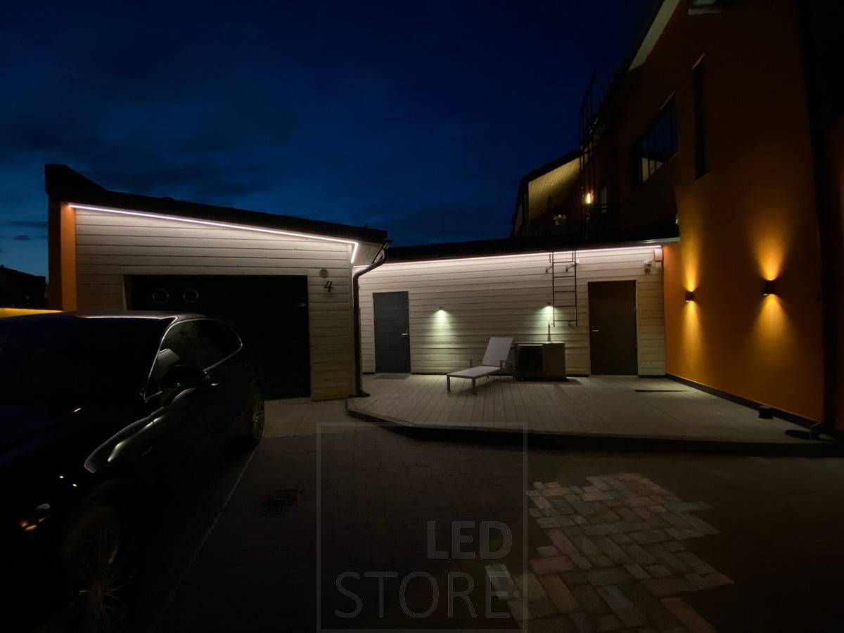 Tira de leds en alero iluminando la fachada de un garaje y almacén con luz indirecta. Además de la iluminación del alero, los apliques de pared iluminan en una y dos direcciones. Ledstore.fi