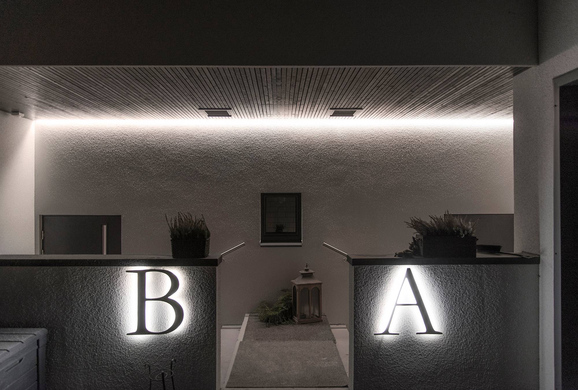 Fachada de una casa iluminada con luz indirecta. Tira de leds instalada en la ranura entre el techo y la pared para iluminar a través de la pared y detrás de las letras grandes para retroiluminación. Ledstore.fi