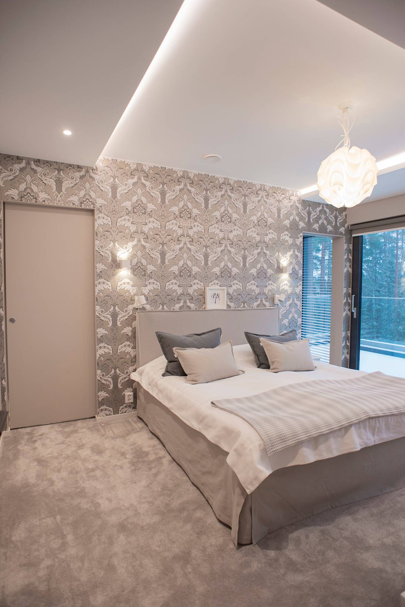 Un dormitorio con una iluminación versátil y propia de un hotel. Iluminación indirecta alrededor de la habitación, iluminación puntual y una lámpara colgante decorativa en el centro de la habitación. Lámparas de pared a ambos lados de la cama. Ledstore.fi