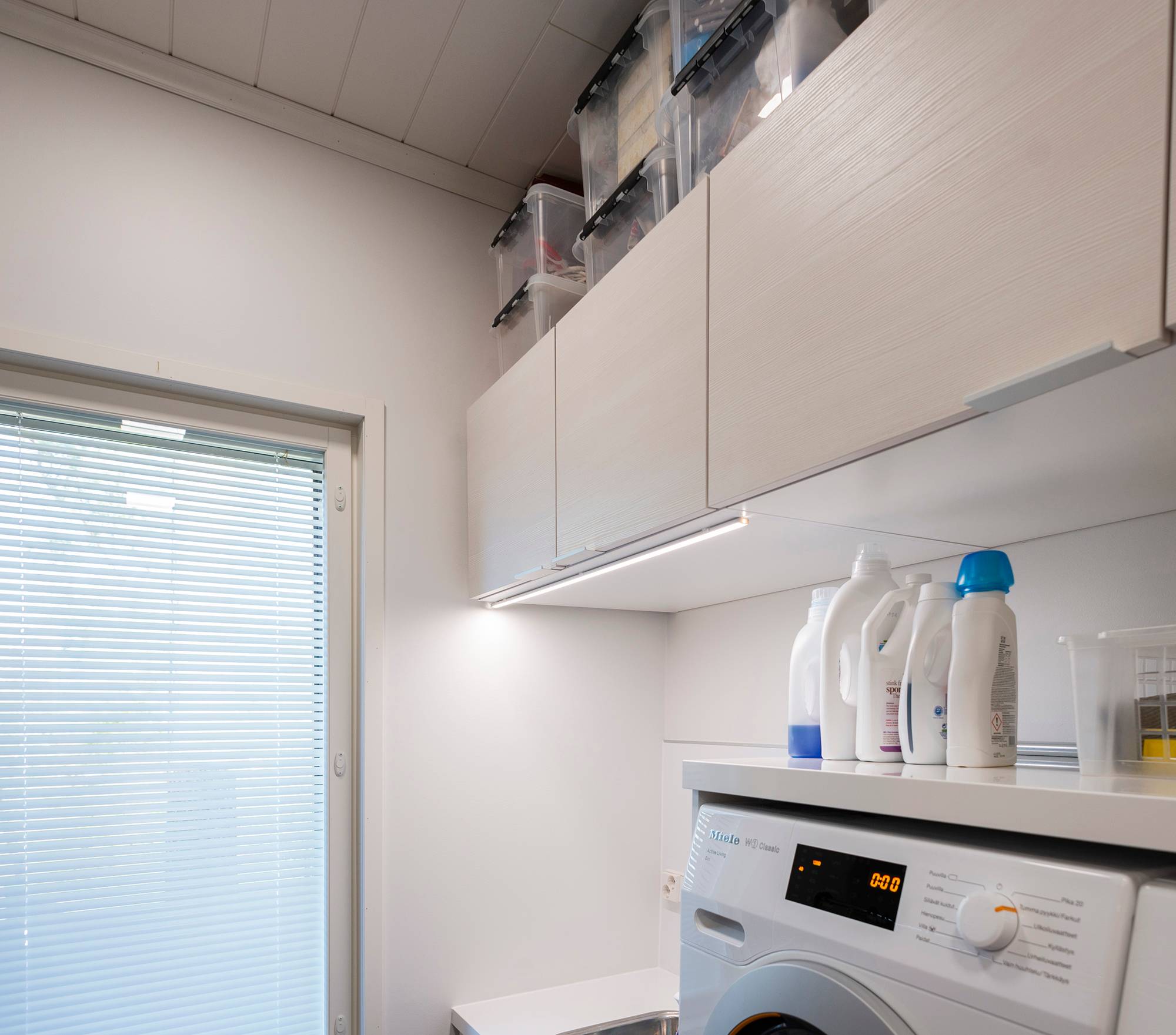 Tira de LED para iluminación adicional en un lavadero, fijada al borde frontal de un armario. Ledstore.fi