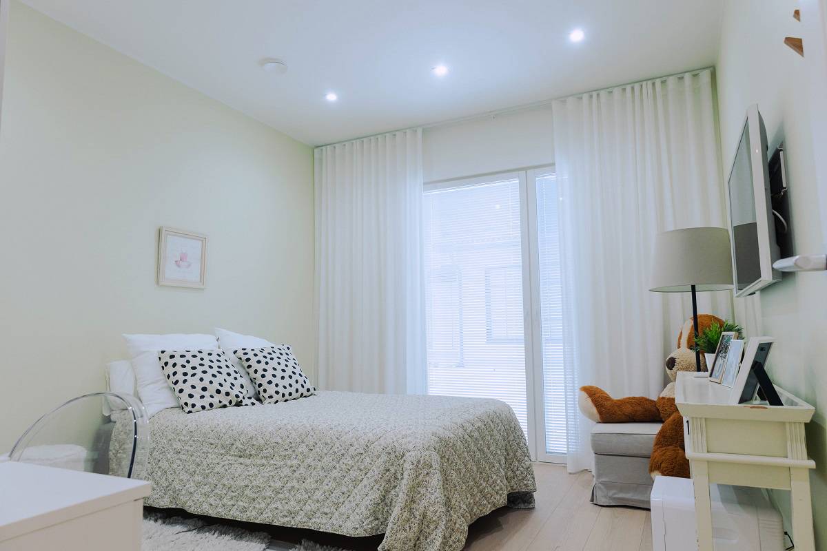 Un dormitorio luminoso y moderno con una cama cuidadosamente hecha, cortinas blancas y una suave iluminación LED. Echa un vistazo a los últimos proyectos de referencia de LedStore.fi para 2025 e inspírate para tu próximo proyecto de interiorismo.