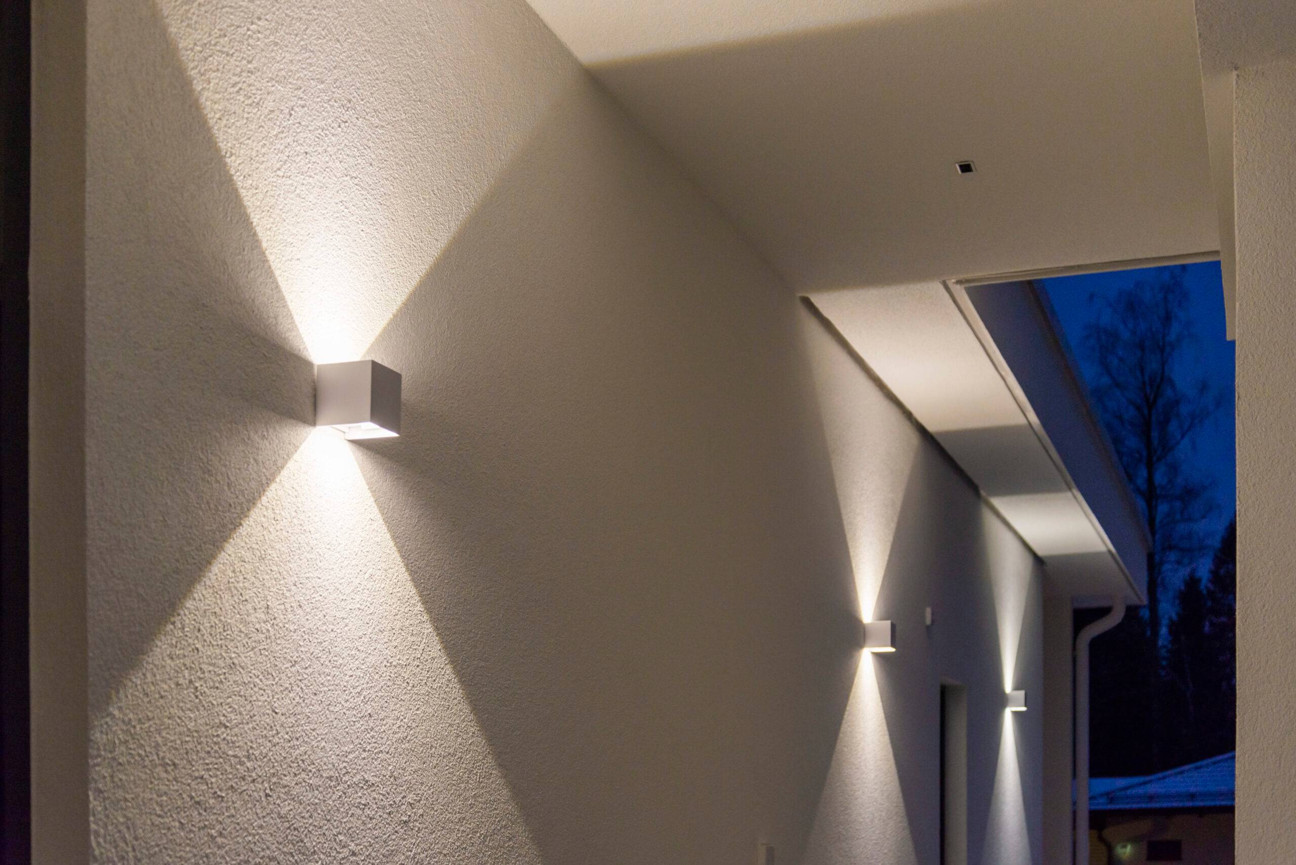 Los apliques LED cúbicos blancos iluminan tanto hacia arriba como hacia abajo, creando un nítido patrón de luz en la pared.