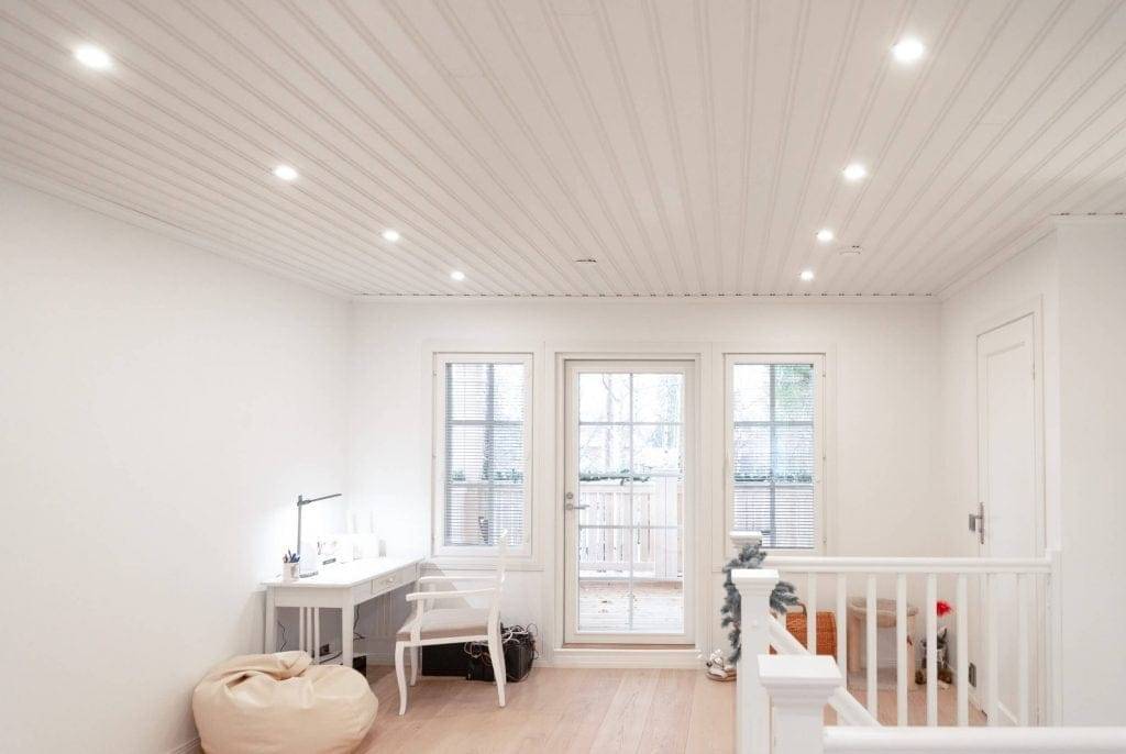 Habitación moderna con iluminación LED empotrada, paredes blancas, escritorio, silla, sillón bean bag, puertas de cristal al balcón; barandilla de la escalera a la derecha.