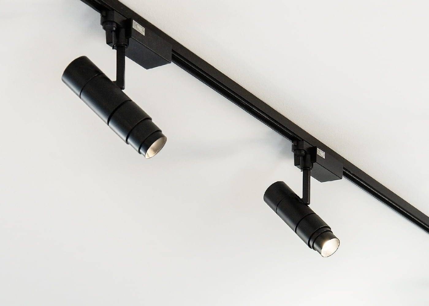 La configuración minimalista con dos luces LED cilíndricas negras de carril sobre un techo blanco, montadas en un riel negro, muestra un diseño de iluminación moderno y ángulos ajustables.