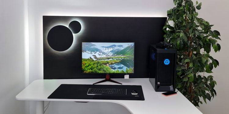 Configuración minimalista de ordenador con escritorio blanco curvado. La pantalla muestra un impresionante paisaje montañoso, iluminado además por retroiluminación LED. A su lado hay una torre de PC negra con detalles LED azules resplandecientes. Este es un ejemplo de cómo las soluciones de iluminación LED de calidad de LedStore.fi pueden dar nueva vida a una oficina en casa o a un espacio de trabajo.