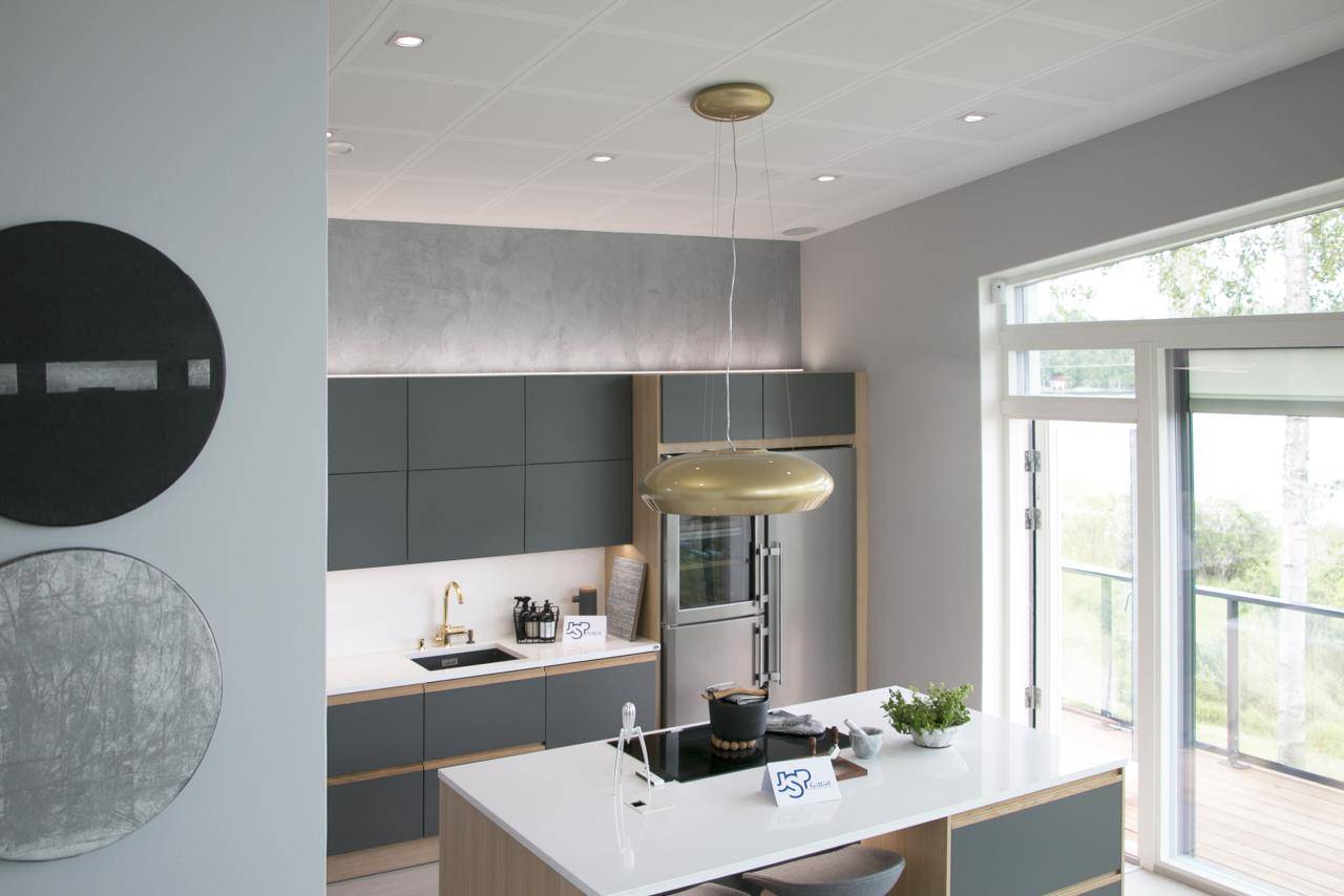 Cocina moderna con armarios verde oscuro, isla blanca, lámparas colgantes doradas y electrodomésticos; arte mural LED que resalta la luz natural de los grandes ventanales.