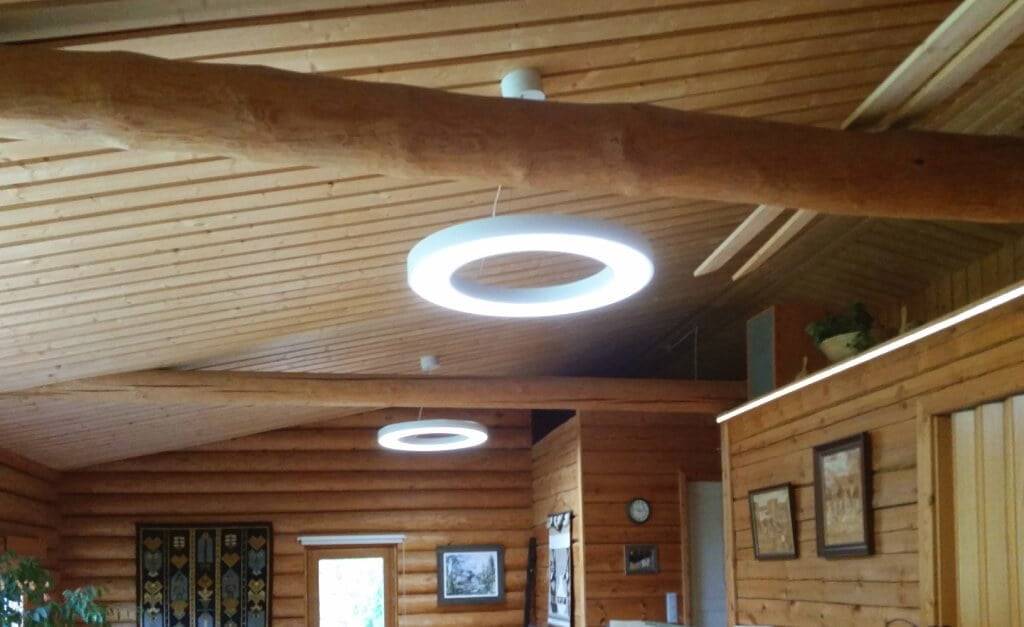 ¿En qué se basan las afirmaciones de que las luces LED son peligrosas? Un interior de madera con luces LED circulares en el techo iluminan el cálido resplandor; las paredes y el techo de troncos crean un encanto rústico con arte enmarcado, un reloj y tapices.