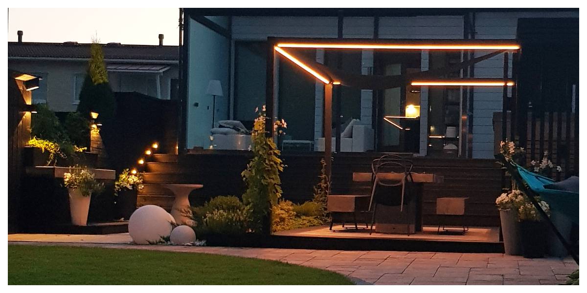 Moderno patio trasero con pérgola e impresionante iluminación ambiental LED. Escalones de madera y plantas en macetas atmosféricas. Situado en el patio de una casa moderna, el conjunto ofrece el escenario perfecto para veladas al aire libre con la iluminación LED de alta calidad de LedStore.fi.  