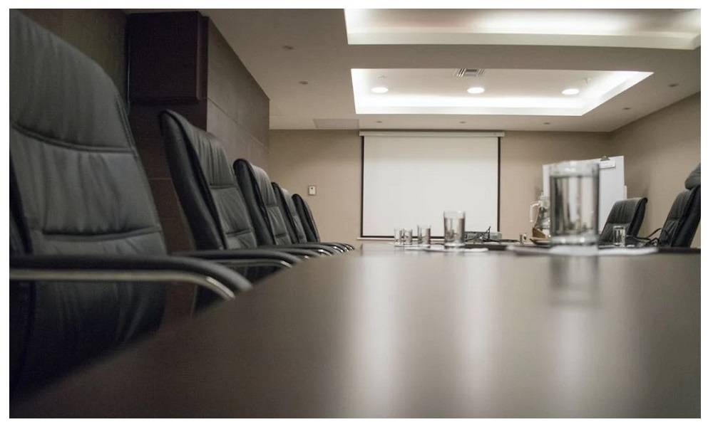 Sala de conferencias con una gran mesa oscura y sillas. Hay varios paneles y focos en el techo.  