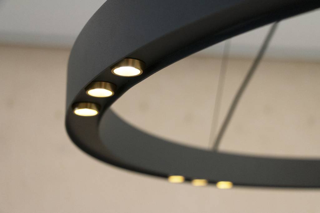 Primer plano de una moderna lámpara de araña redonda en negro mate con luces LED empotradas que crean un suave resplandor sobre un fondo difuminado para crear un ambiente elegante.