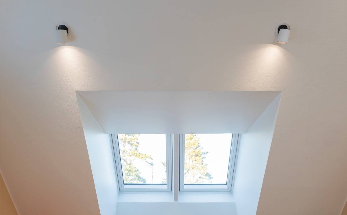 Arriba, dos apliques orientables en la pared de la habitación con techo inclinado.