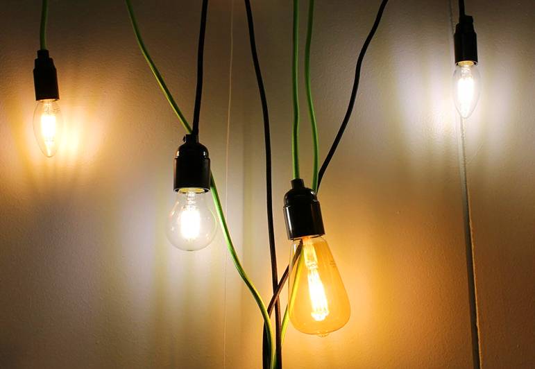 Los cables negros y verdes de cuatro elegantes lámparas LED cuelgan de una pared clara, para un interior moderno.