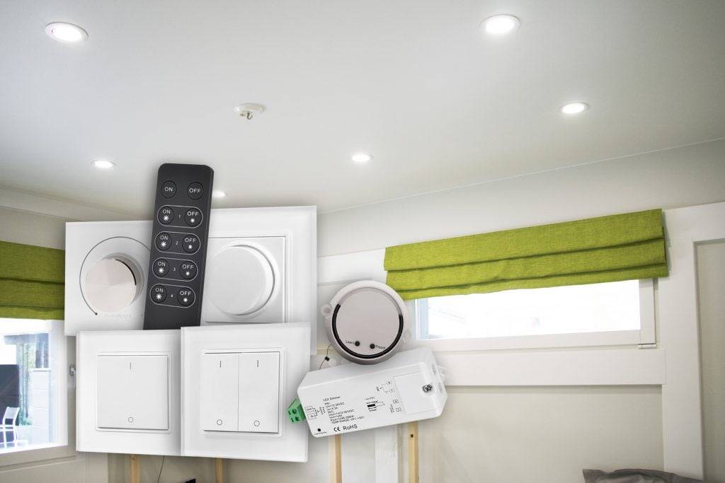 La sala tiene luces LED empotradas en el techo, persianas verdes en la ventana y diversos interruptores eléctricos y mandos a distancia a la vista.