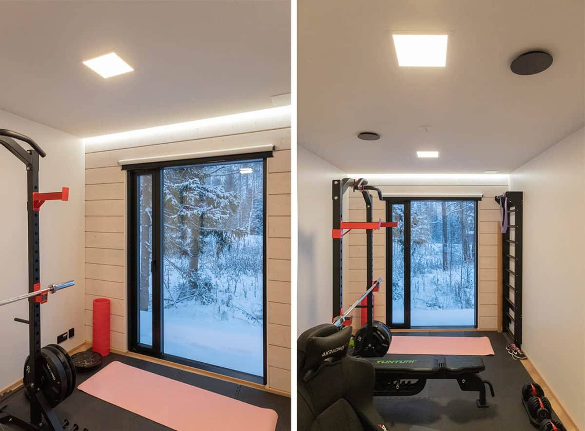 Un pequeño gimnasio con una gran ventana al exterior, dos pequeños paneles luminosos en el techo y una tira de leds encima de la ventana.
