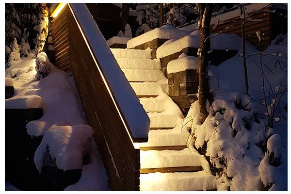 Escaleras cubiertas de nieve al anochecer, con una luz cálida que brilla desde la barandilla sobre las escaleras.  