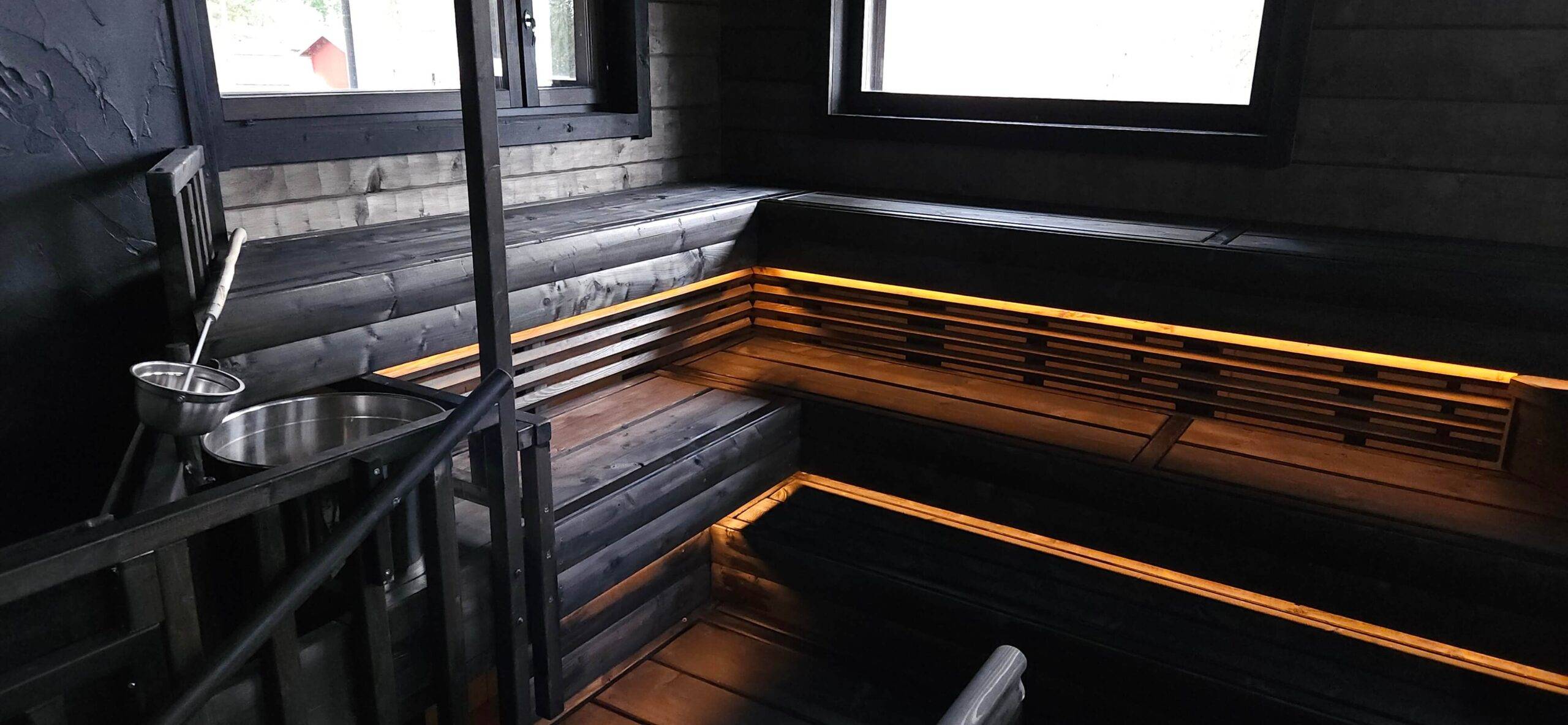 en la parte inferior del techo de madera oscura de la sauna, se instalaron tiras de luces LED de color amarillento cálido para iluminar hacia abajo