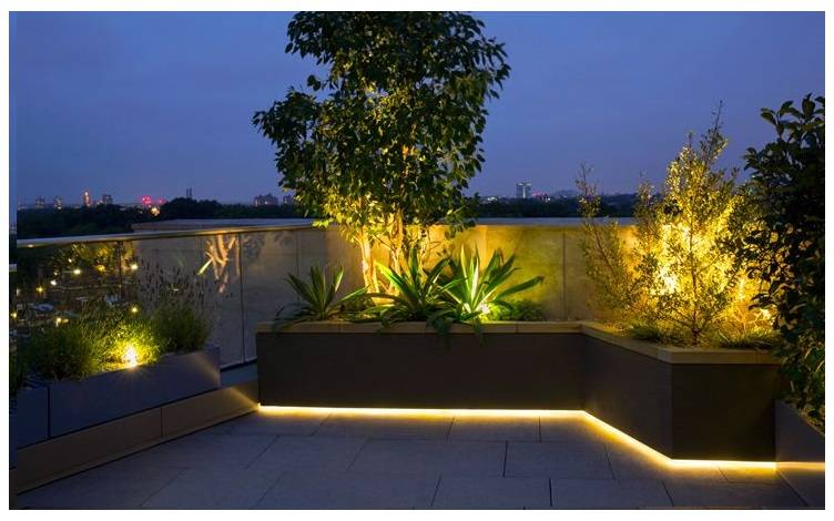 Parterre elevado iluminado desde abajo con una tira de LED de color cálido. El parterre también tiene otros focos de luz de tonos cálidos.  