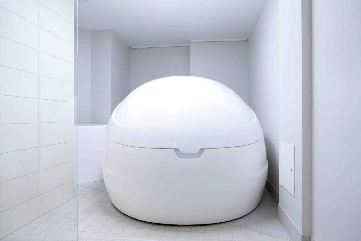 La tienda online LedSto.fi presenta un gran tanque blanco ovalado de estimulación sensorial, situado en un espacio minimalista con paredes y suelo de baldosas. Las suaves luces LED resaltan la superficie lisa y la tapa cerrada del tanque, destacando su diseño para terapia de aislamiento o flotación.